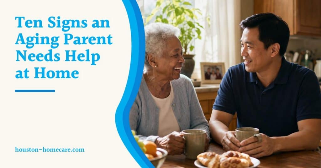 A smiling older woman and her male caregiver chat over coffee at a sunny kitchen table at home.